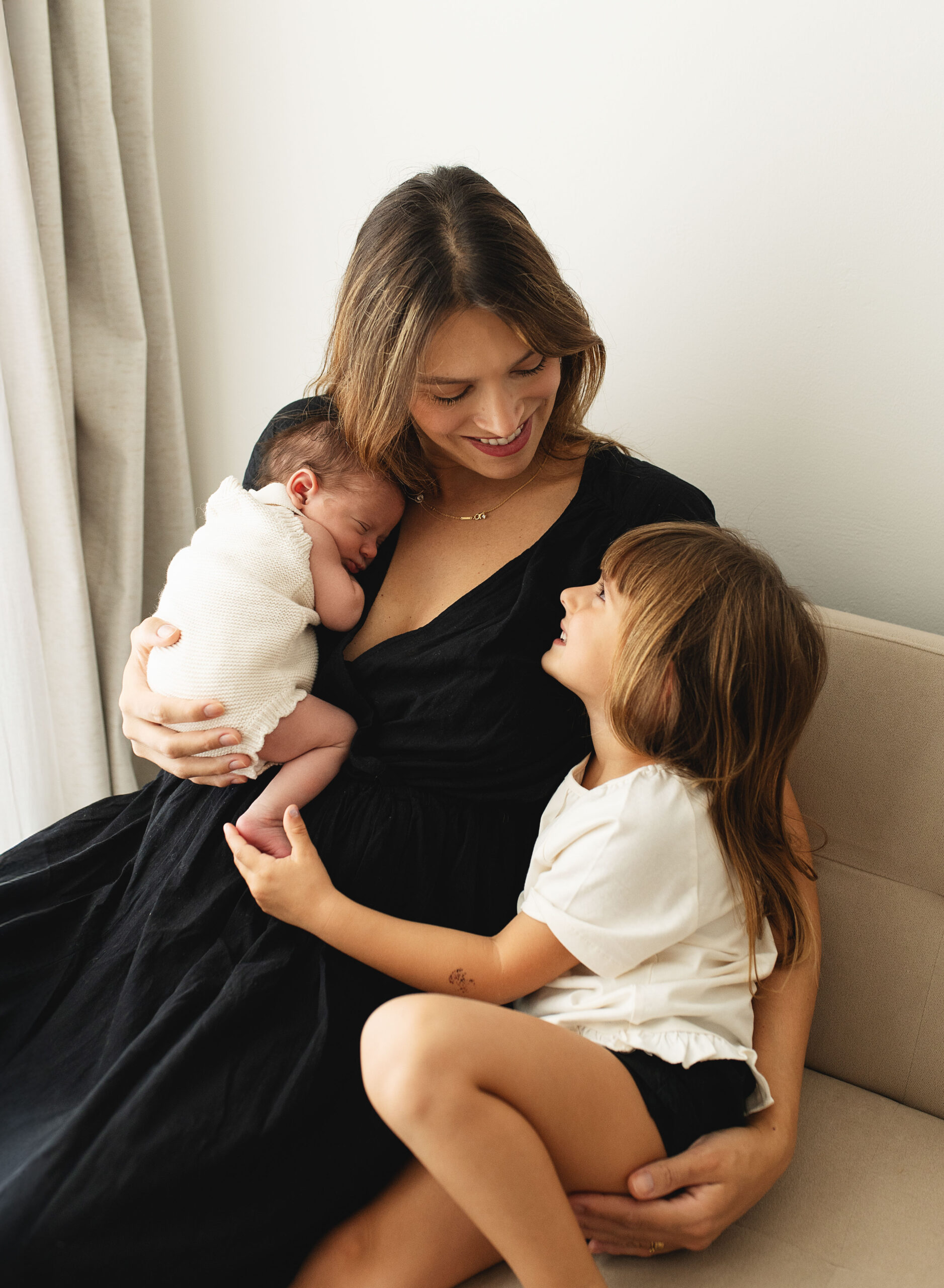 Mother cradling her newborn baby whilst cuddling her elder daughter at their newborn photoshoot in Poole, Dorset